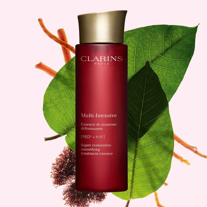 Kuva Clarins Super Restorative Treatment Essence esanssista, Jania rubensista, harunganan lehdistä ja ginsengin juurista vaaleanpunaista taustaa vasten.