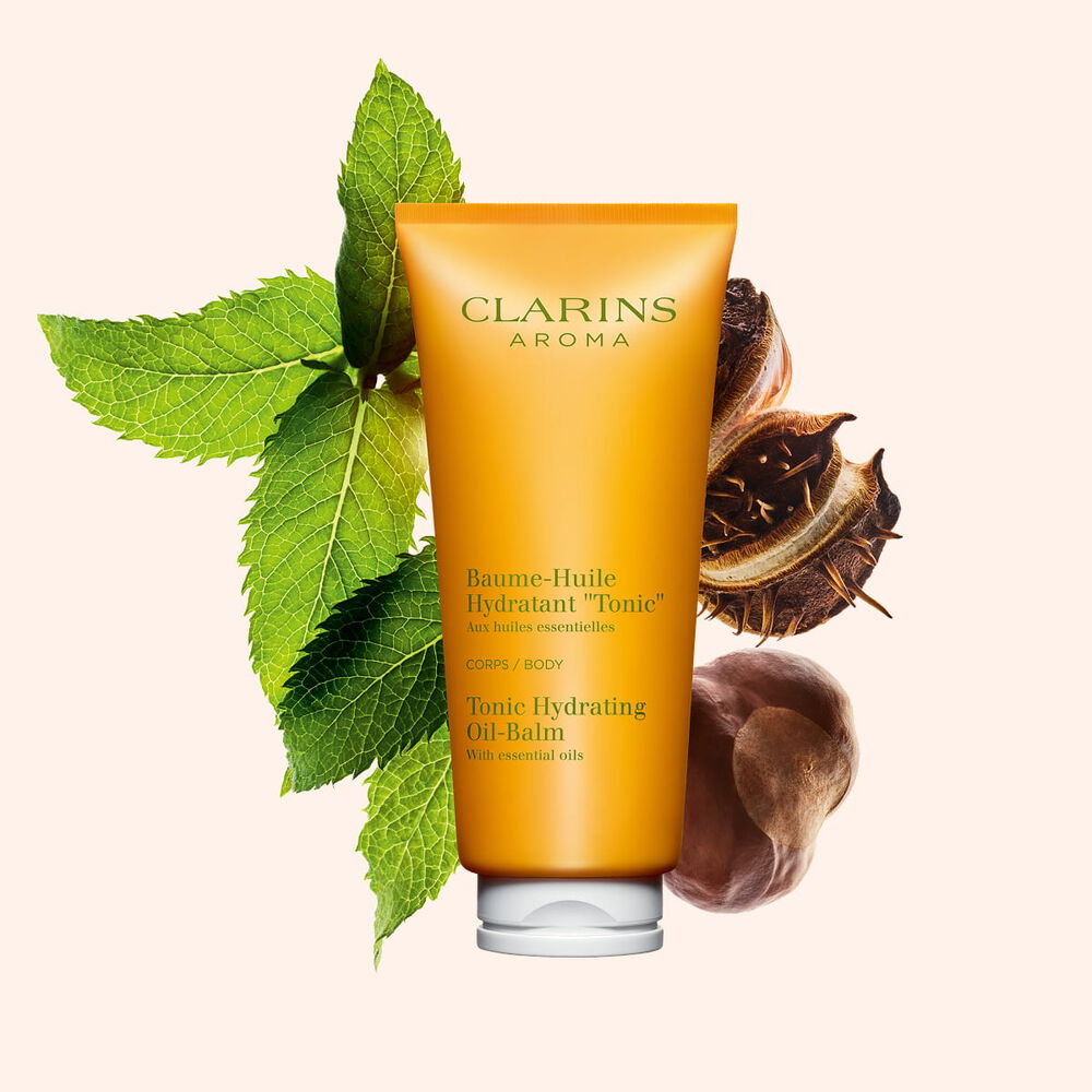 Kuva Clarins Tonic Hydrating Oil-balm tuubi, mintunlehti&auml; ja karitepuun p&auml;hkin&ouml;it&auml; persikanv&auml;rist&auml; taustaa vasten.