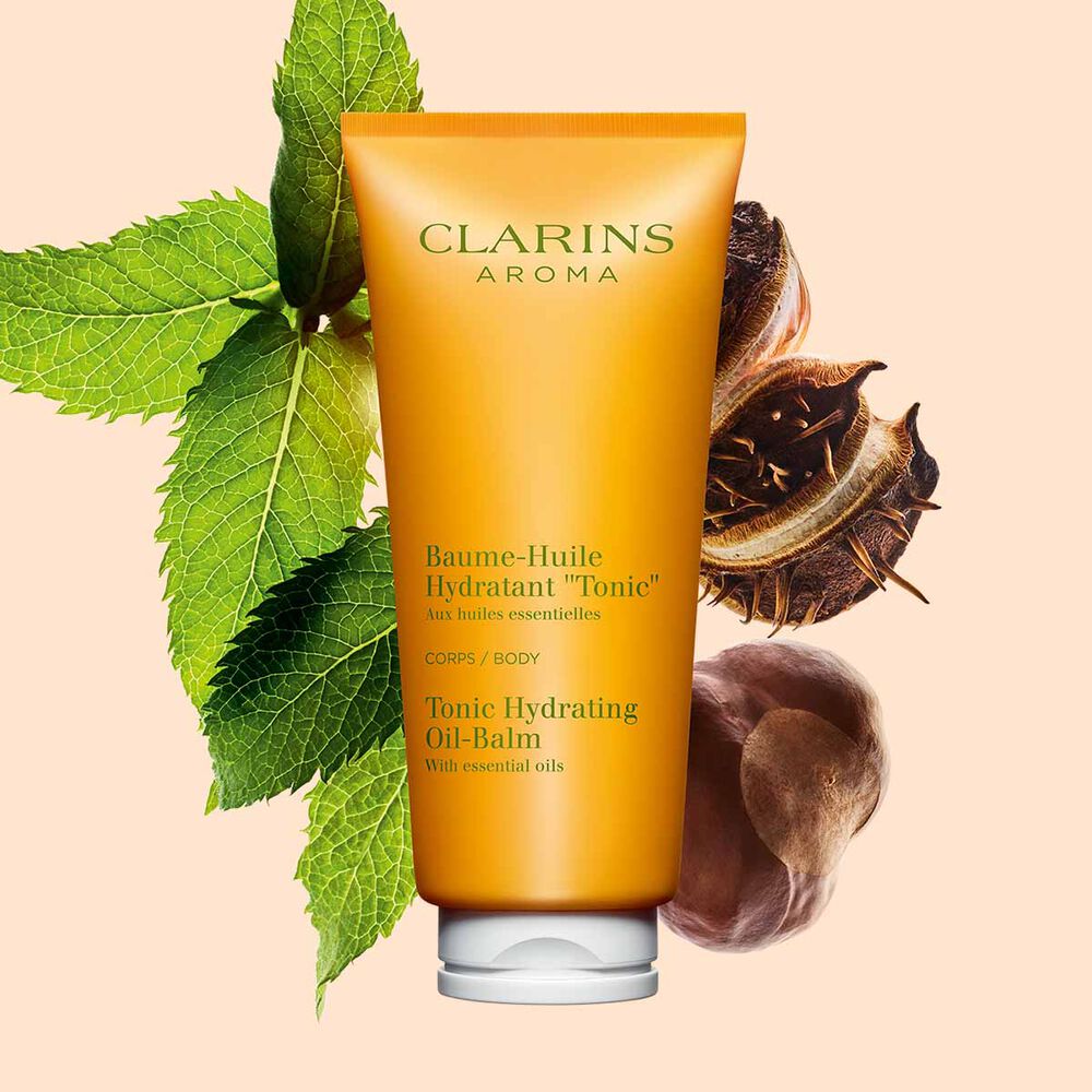 Kuva Clarins Tonic Hydrating Oil-balm tuubi, mintunlehtiä ja karitepuun pähkinöitä persikanväristä taustaa vasten.