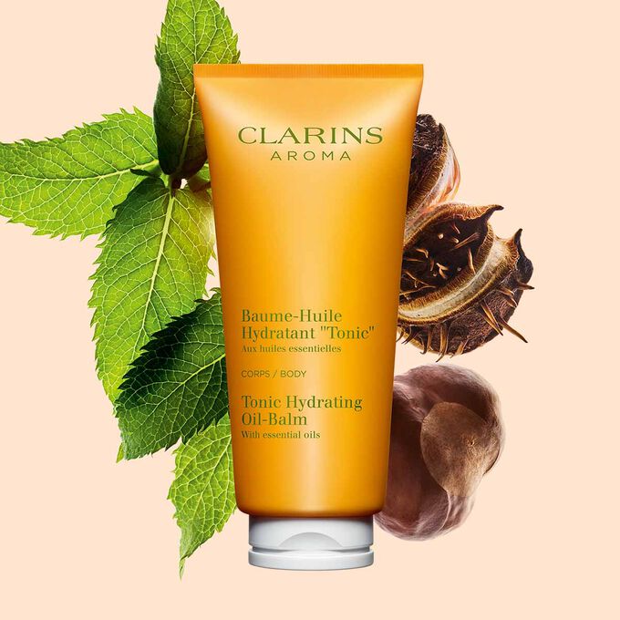 Kuva Clarins Tonic Hydrating Oil-balm tuubi, mintunlehtiä ja karitepuun pähkinöitä persikanväristä taustaa vasten.