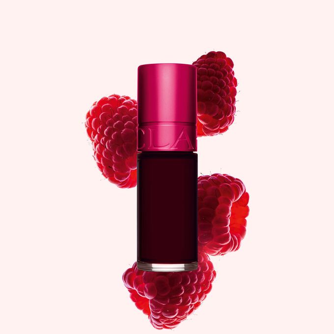 Packshot Clarins Pink Water Lip Stain -huuliv&auml;rist&auml; s&auml;vyss&auml; 04, asetettuna vadelmien viereen vaaleanpunaiselle taustalle.
