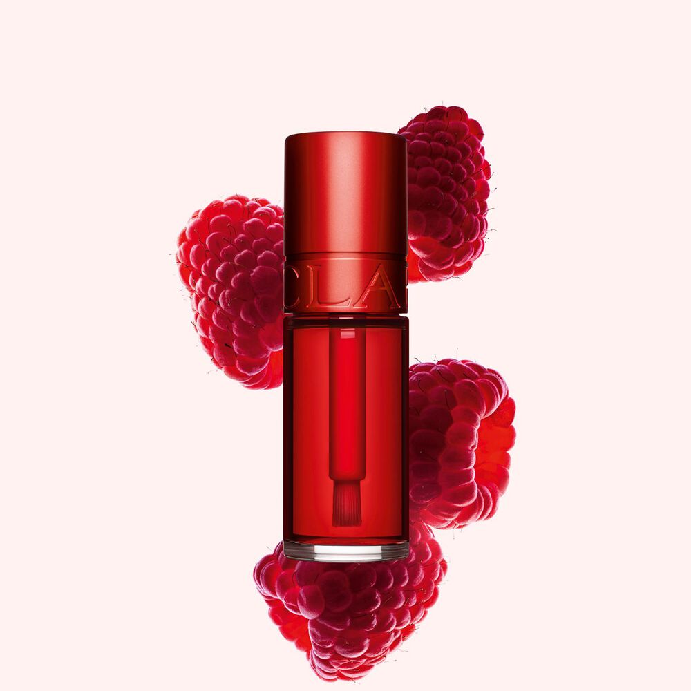 Packshot Clarins Red Water Lip Stain -huuliv&auml;rist&auml; s&auml;vyss&auml; 03, asetettuna vadelmien viereen vaaleanpunaiselle taustalle.
