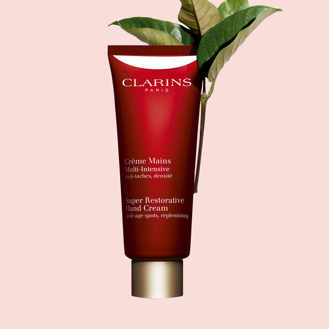Kuva Clarins Super Restorative Hand Cream pullosta ja harunganan lehdistä vaaleanpunaista taustaa vasten.