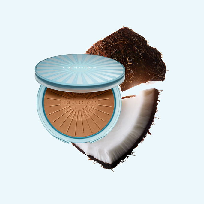 Summer Bronzing Powder -aurinkopuuterin tuotekuva kookoksen ymp&auml;r&ouml;im&auml;n&auml;, korostaen sen keskeist&auml; ainesosaa luonnolliseen, auringon suutelemaan hehkuun