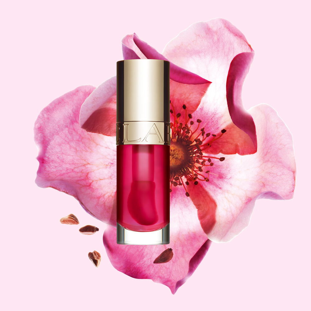 Packshot Clarins Lip Comfort Oil -tuotteesta Pitaya, asetettuna l&auml;helle ruusunmarjaa vaaleanpunaiselle taustalle.