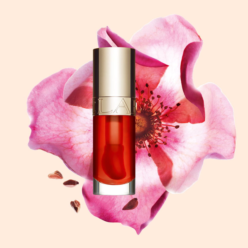 Packshot Clarins Lip Comfort Oil Apricot -s&auml;vysta, asetettuna ruusunmarjakukan viereen vaalean oranssilla persikkataustalla.