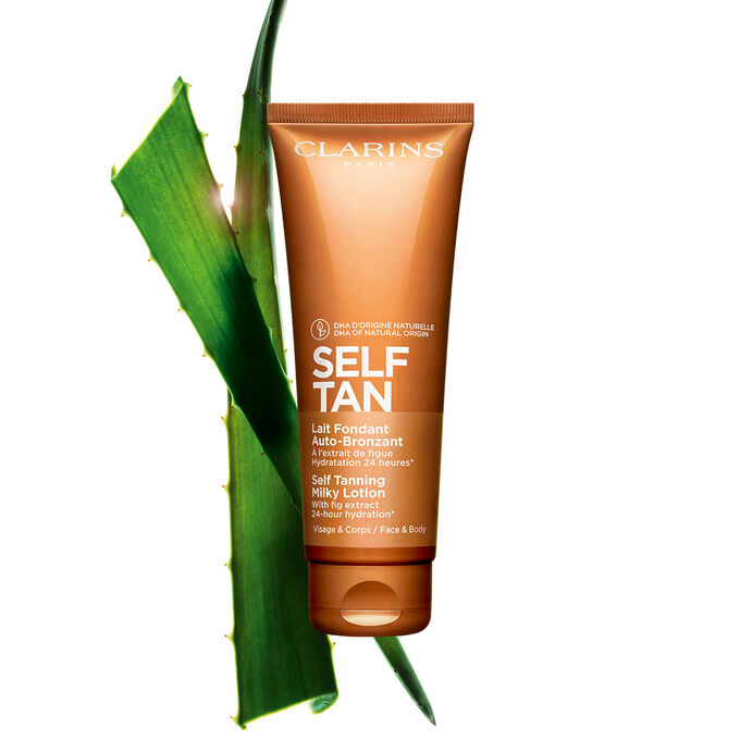 Kuva Clarins Self Tanning Milky Lotion tuubista ja aloe veran lehdest&auml; vaaleanoranssia taustaa vasten.
