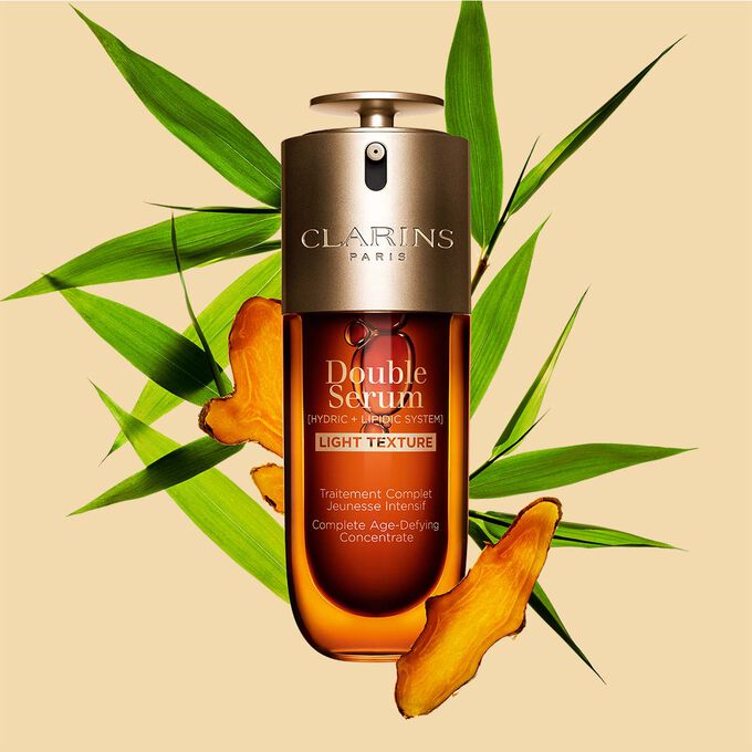 50 ml:n pullo Clarinsin Double Serum Light Texturea, kurkuma- ja jättiruokolehtiä oranssia taustaa vasten.