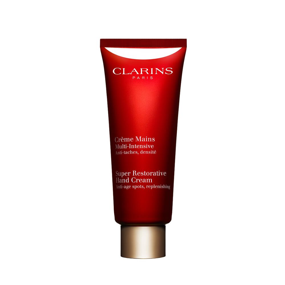 Kuva Clarins Super Restorative Hand Cream pullosta ja harunganan lehdist&auml; vaaleanpunaista taustaa vasten.