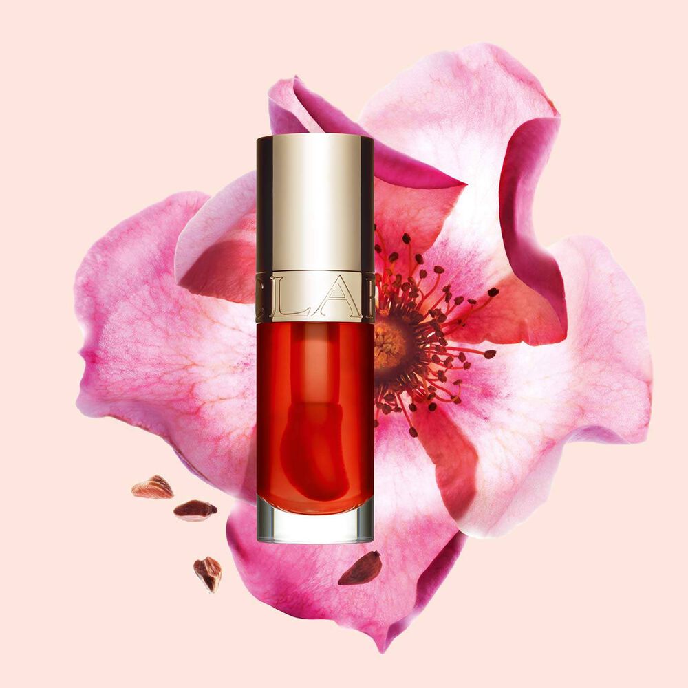 Packshot Clarins Lip Comfort Oil Apricot -sävysta, asetettuna ruusunmarjakukan viereen vaalean oranssilla persikkataustalla.
