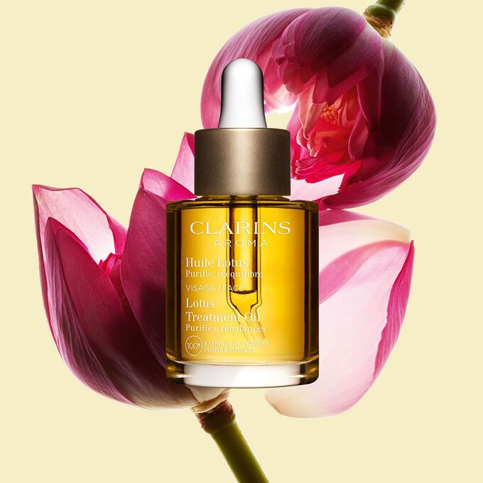 Kuva Clarins Lotus Face Treatment Oil pullosta ja lootuksenkukasta vaaleankeltaista taustaa vasten.