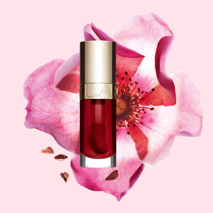 Packshot Clarins Lip Comfort Oil -huuli&ouml;ljyst&auml; s&auml;vy Cherry, sijoitettuna ruusunmarjan viereen vaaleanpunaiselle taustalle.