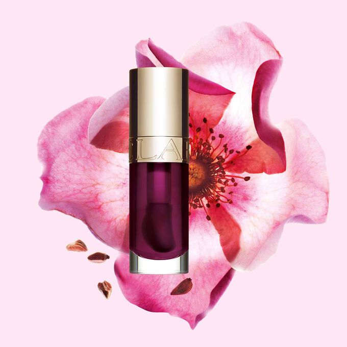 Packshot Clarins Lip Comfort Oil -tuotteesta sävyssä Plum, sijoitettuna ruusunmarjakukan vierelle vaaleanpunaiselle taustalle.