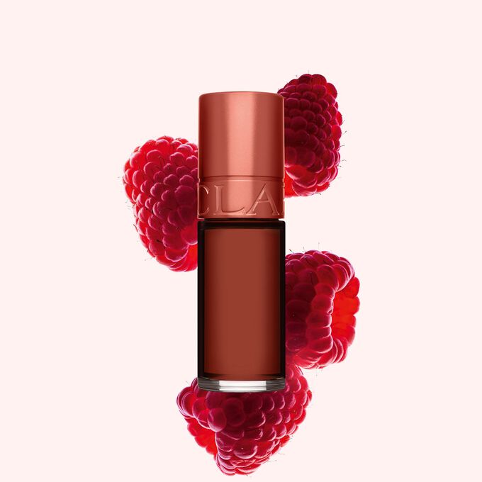 Packshot Clarins Brown Water Lip Stain -huuliv&auml;rist&auml; s&auml;vyss&auml; 13, asetettuna vadelmien viereen vaaleanpunaiselle taustalle.